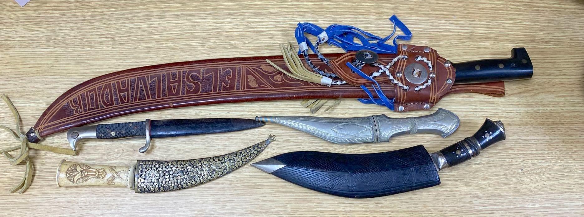 Five various weapons including a Kukri, a carved bone handled dagger with brass sun, moon and stars sheath and an El Salvador machete